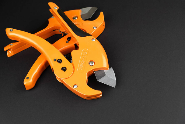 orange scissors for cutting propylene pipes on a black background - Фото, изображение