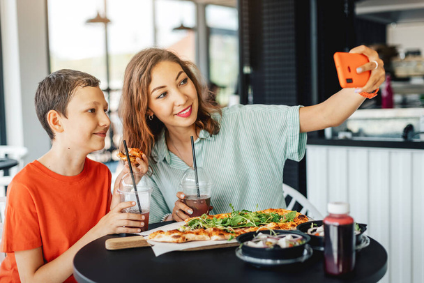 Madre e figlio si divertono in un caffè mangiando pizza e scattando selfie su uno smartphone per i social network - Foto, immagini