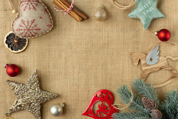 Beautiful Christmas decorations in vintage style, a spruce branch and golden star are located around the perimeter against a burlap background. Free space for text. View from the top point. - Photo, Image
