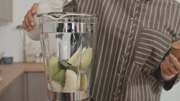 Κοντινό πλάνο της γυναίκας ρίχνει γάλα στο μπλέντερ με φρέσκα φρούτα σε αυτό, ενώ κάνοντας smoothie στο σπίτι - Πλάνα, βίντεο