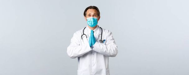 Covid-19, ehkäisy virus, terveydenhuollon työntekijöiden ja rokotus käsite. Toiveikas lääkäri lääketieteellisessä naamiossa ja käsineet kädestä rukoillen, rypistäen otsaansa kerjääen, rukoillen palvelusta - Valokuva, kuva