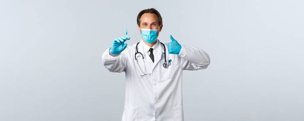 Covid-19, prevención de virus, trabajadores sanitarios y concepto de vacunación. Médico profesional de confianza en máscara médica y guantes thumbs-up, recomienda la vacuna contra el coronavirus, la celebración de la jeringa
 - Foto, Imagen