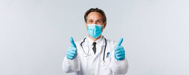 Covid-19 、ウイルス、医療従事者および予防接種の概念を防止する。医療用マスクと手袋の満足医師のクローズアップ,親指アップを表示,提供されるサービスの保証品質,お勧めします製品 - 写真・画像