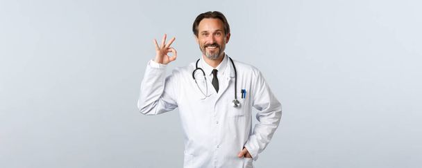 Ковід-19, спалах коронавірусу, медичні працівники та концепція пандемії. Впевнений чоловік-лікар, професійний терапевт у клініці показують добре жест, який рекомендує або гарантує якість
 - Фото, зображення