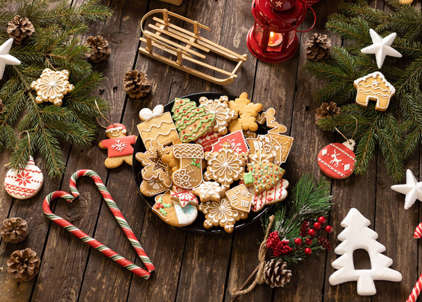 Cookies, candy and biscuits in festive winter holiday shapes nicely arranged on a plate placed on a wooden table with Christmas decoration and ornaments, winter holidays concept - Фото, изображение