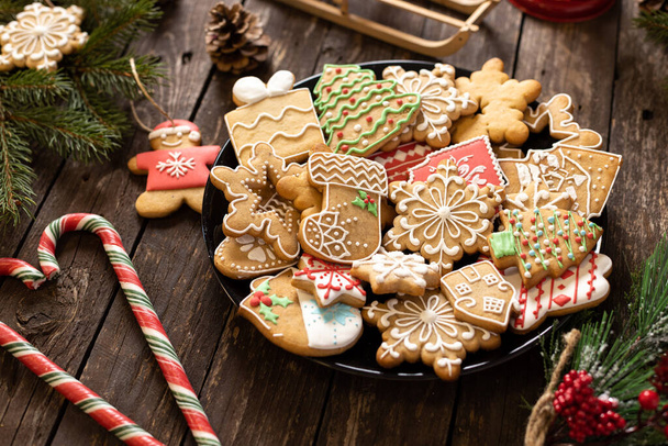 Plate full of traditionally shaped Christmas cookies glazed in sugar icing winter holiday themes placed on a wooden table decorated in concept of Christmas and New Year   - Фото, зображення