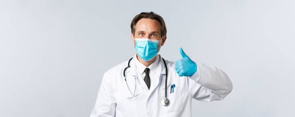 Covid-19 、ウイルス、医療従事者および予防接種の概念を防止する。興奮した幸せな医師の笑顔熱狂的な、医療用マスクと手袋を着用親指アップ、同意または承認製品を表示 - 写真・画像