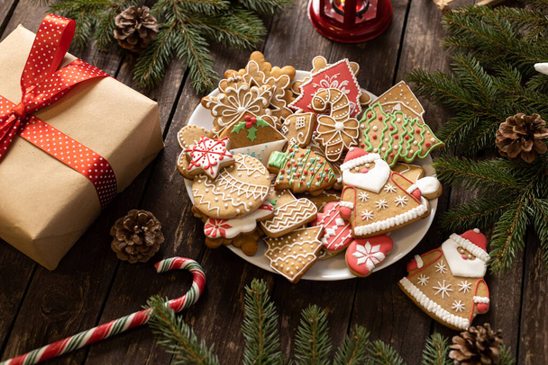 Christmas cookies in various festive shapes on the plate alongside conifer branches placed upon rustic wooden background concept - Фото, зображення