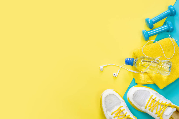yellow background on a sports theme, blue dumbbells, sneakers, headphones, water - Zdjęcie, obraz