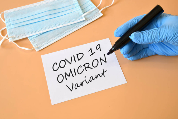 Covid-19 'un yeni Omicron versiyonu. Mavi eldivenli doktor elinde beyaz kağıt ve "Covid-19 Varyant Omicron" yazılı bir kalem tutuyor. Tıbbi yüz maskesi. Yeni Covid 19 Omicron varyantı için koruma konsepti. Boşluğu kopyala. - Fotoğraf, Görsel