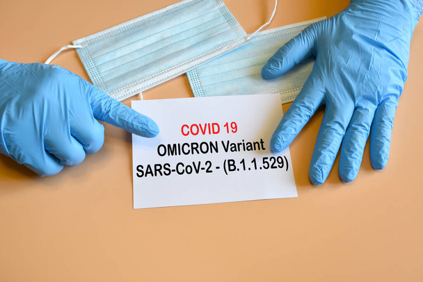 Covid-19 'un yeni Omicron versiyonu. Mavi eldivenli doktor eli beyaz kağıda "Covid-19 Varyant Omicron" yazmış. Covid 19 virüsünün korunması için tıbbi yüz maskeleri. Yeni Covid 19 Omicron varyantı için koruma kavramı - Fotoğraf, Görsel