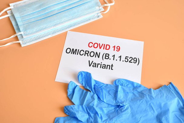 Covid-19 'un yeni Omicron versiyonu. Tıbbi yüz maskeleri, üzerinde "Covid-19 Varyant Omicron" yazan beyaz kağıtlı mavi tıbbi eldivenler. Covid 19 virüsünün yeni Omicron varyasyonundan koruma kavramı. - Fotoğraf, Görsel