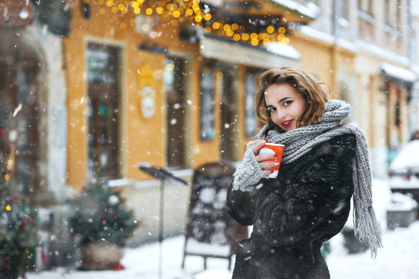 Encantadora joven bebiendo café en la ciudad durante las nevadas. Espacio vacío - Foto, Imagen
