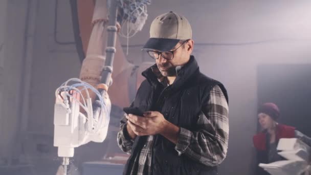 Férfi kézműves okostelefon közelében robotkar - Felvétel, videó