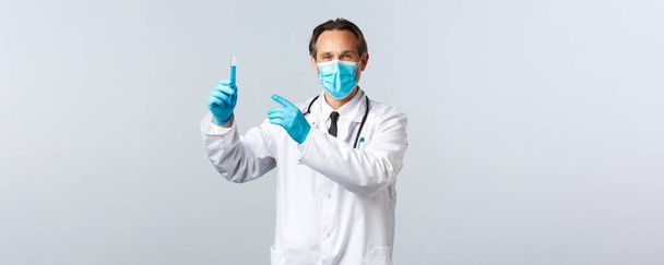 Covid-19 、ウイルス、医療従事者および予防接種の概念を防止する。医療用マスクと手袋で満足笑顔の医師ワクチンサンプルで検査管を指して、薬を承認 - 写真・画像
