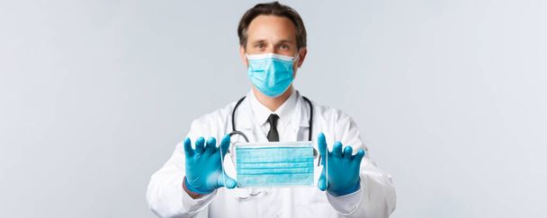 Ковід-19, вірус, працівники охорони здоров'я та концепція вакцинації. Лікар середнього віку в PPE, рекомендує бренд медичної маски, пояснює, як носити маску, щоб запобігти захворюванню коронавірусу. - Фото, зображення