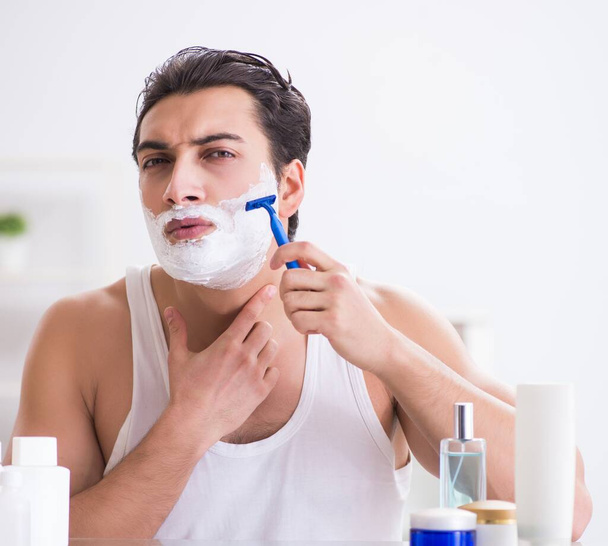 Fiatal jóképű férfi borotválkozik korán reggel otthon. - Fotó, kép