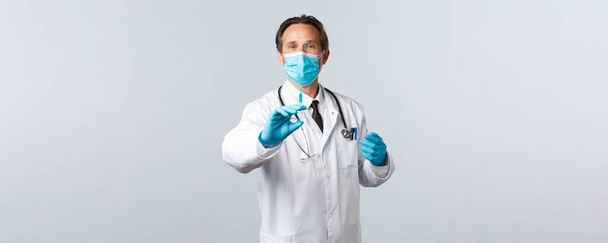 Covid-19 、ウイルス、医療従事者および予防接種の概念を防止する。医療用マスクと手袋を保持注射器で中年の医師は、コロナウイルスワクチンやHIV準備と、患者のために撮影準備 - 写真・画像