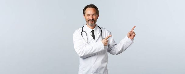 Ковід-19, спалах коронавірусу, медичні працівники та концепція пандемії. Дружній усміхнений красивий чоловік-лікар, який показує промо, носить біле пальто і стетоскоп, поради приймають ці ліки
 - Фото, зображення
