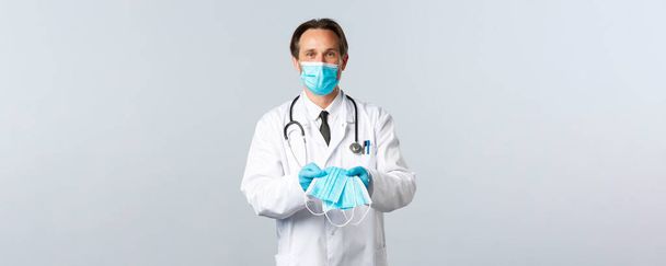 Covid-19, virüsü önleme, sağlık çalışanları ve aşı konsepti. PPE 'deki faydalı erkek doktor hasta Coronavirus hastalarına tıbbi maske veriyor. - Fotoğraf, Görsel