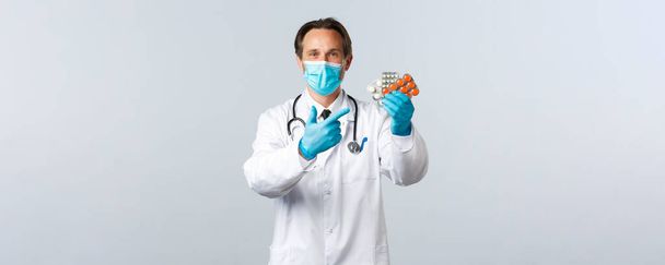 Covid-19, virüsü önleme, sağlık çalışanları ve aşı konsepti. Eczacı ilaç öneriyor. Tıbbi maskeli doktor ve eldivenler hapları gösteriyor, ilaç yazıyor. - Fotoğraf, Görsel