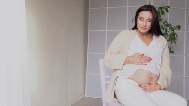 mooie zwangere vrouw thuis in een witte kamer wachten op een baby - Video
