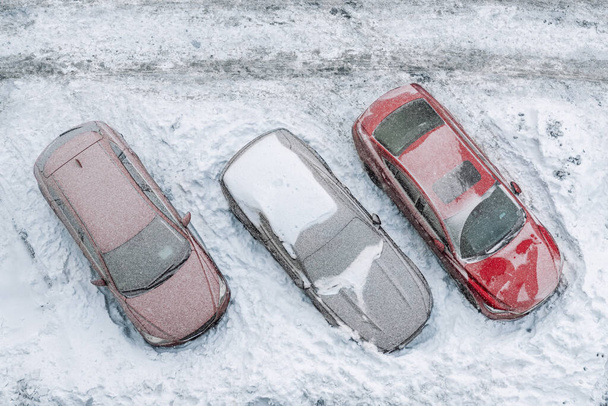 Horní letecký pohled na byt kancelářské budovy parkoviště s mnoha vozy pokryté sněhem přilepený po silné sněhové bouři zimní den. Sněhové závěje a zamrzlá vozidla. Extrémní klimatické podmínky - Fotografie, Obrázek