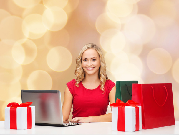 smiling woman in red shirt with gifts and laptop - Photo, Image