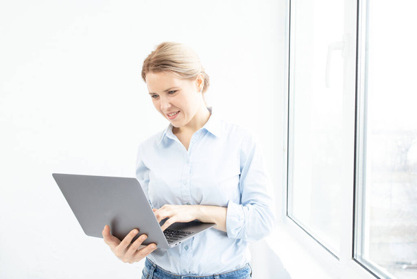 Successful young woman using laptop near the window. Confident girl, freelancer, manager at work at home or office. Business, remote work, career, online teacher or doctor, distance education concept. - Fotó, kép