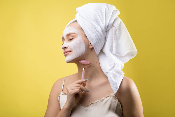 Chica con una máscara cosmética en su cara en una toalla blanca. - Foto, Imagen