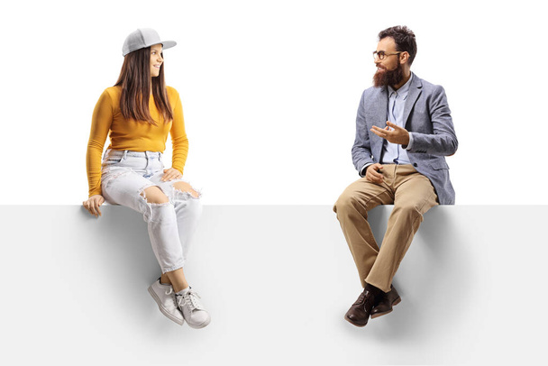 Bearder man talking to a young casual female seated on a blank panel isolated on white background - Foto, Bild