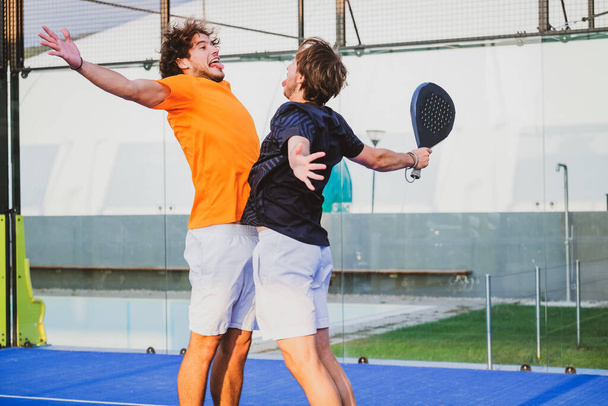 Portrait de deux sportifs souriants posant sur le terrain de padel en plein air avec des raquettes - Joueurs Padel embrassant après avoir gagné un match de padel - Photo, image