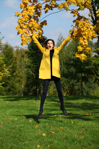 Happy woman in yellow coat jumping in autumn park - Foto, immagini