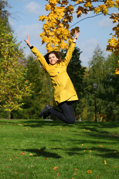 Happy woman in yellow coat jumping in autumn park - Fotoğraf, Görsel