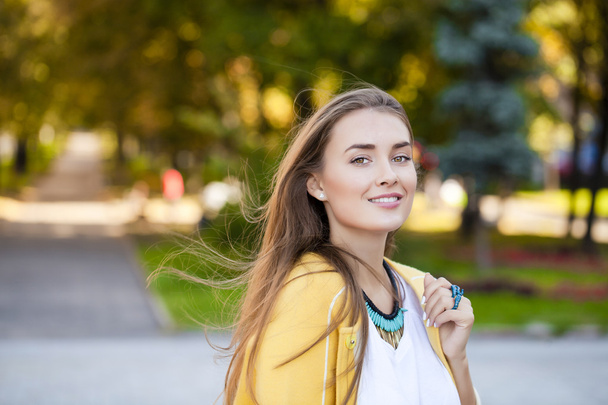 Happy young woman in yellow coat in autumn street - Фото, изображение
