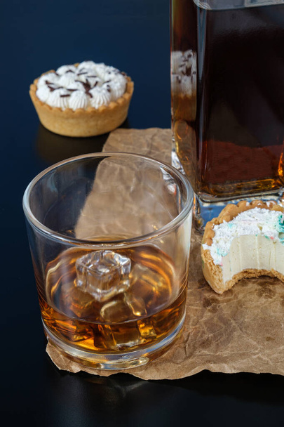 Стакан виски на льду, рядом с мини-пирогом, с кусочком, с белым шоколадом ганач. - Фото, изображение