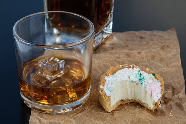 Мини-пирог с белым шоколадом ганач, с укусом, рядом со стаканом виски на льду. - Фото, изображение