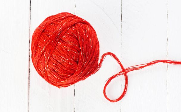 a ball of red yarn on a white background of painted boards close-up. - Valokuva, kuva