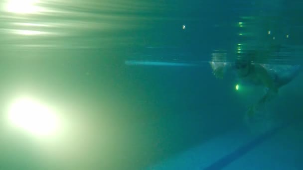 Młody brodaty mężczyzna w wodoodpornych okularach pływa pod wodą - odpycha się nogami z boku i odwraca - Materiał filmowy, wideo