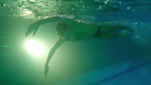 Młody brodaty mężczyzna w wodoodpornych okularach pływa pod wodą - odpycha się nogami z boku i zawraca na tor - Materiał filmowy, wideo