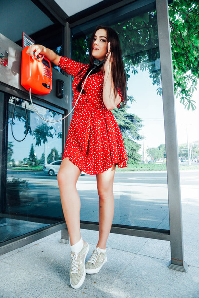 beautiful brunette woman in red dress talking payphone - Фото, зображення