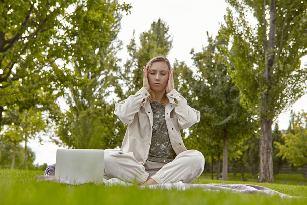 A woman sits cross-legged in the lotus position Sukhasana and meditates in the park. Attractive woman relieves stress by meditating in the park - Photo, Image