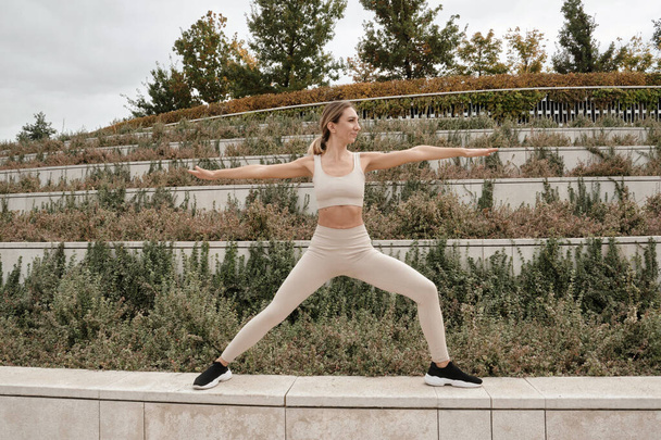 Une athlète blonde d'âge moyen, blanche et vêtue d'un haut beige et de leggings pratique le yoga asanas dans un parc de la ville. Harmonie et paix. Cours de yoga en plein air. - Photo, image