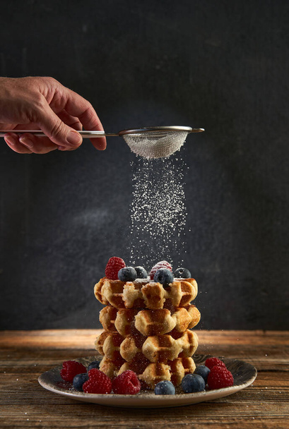Woman's hand sprinkling powder sugar on a stack of waffles with fresh berries on them - Foto, Imagem