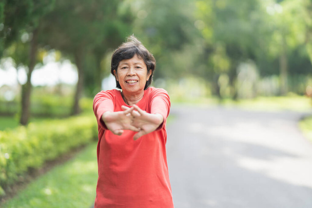 Mujer asiática mayor calentamiento corporal antes de hacer ejercicio. Vieja mujer estirándose antes de correr en el jardín, Deporte atleta corriendo concepto. - Foto, imagen