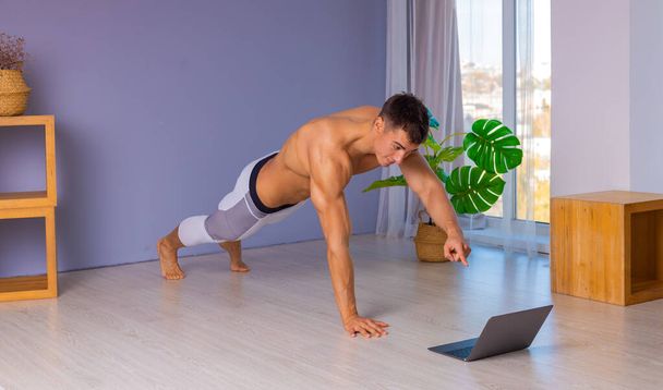 Online trainer. On-line sports. fitness and healthy lifestyle concept. Man with laptop computer doing plank exercise at home during a pandemic. - Fotó, kép