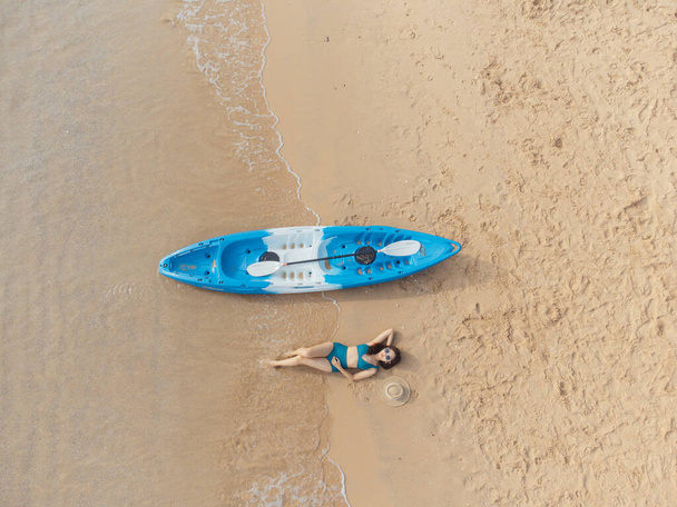Beautiful woman in bikini lying on the beach with a kayak beside - Fotoğraf, Görsel