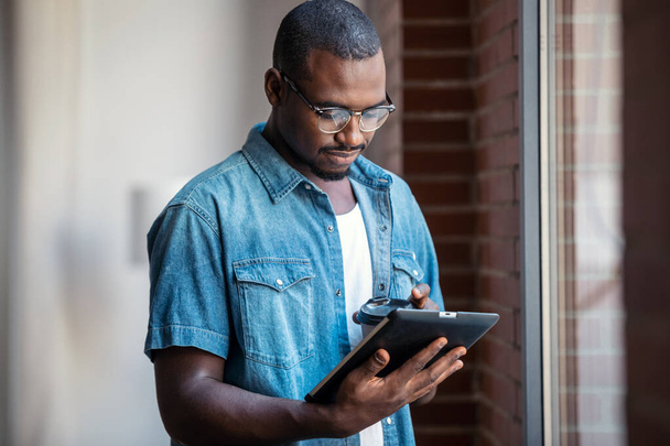 Prise de vue d'un homme d'affaires confiant travaillant avec une tablette numérique tout en se tenant près des fenêtres dans un espace de coworking. - Photo, image