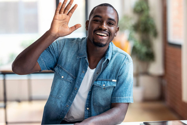 Portrait of afro-american business man entrepreneur looking at camera while waving hand in a modern startup. - 写真・画像