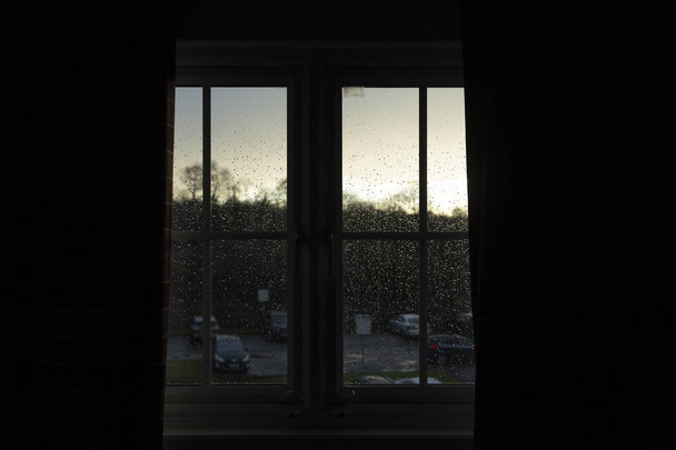 雨滴が英国マンチェスター空港近くのホテルの部屋の窓のガラスに固執しながら、その日の最後のライトは、嵐の後にフィルタ - 写真・画像